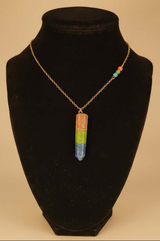Celebrate polysexual pride with a handcrafted resin pendant filled with rhodonite, peridot, and lapis gemstone sand. On Gold plated chain.